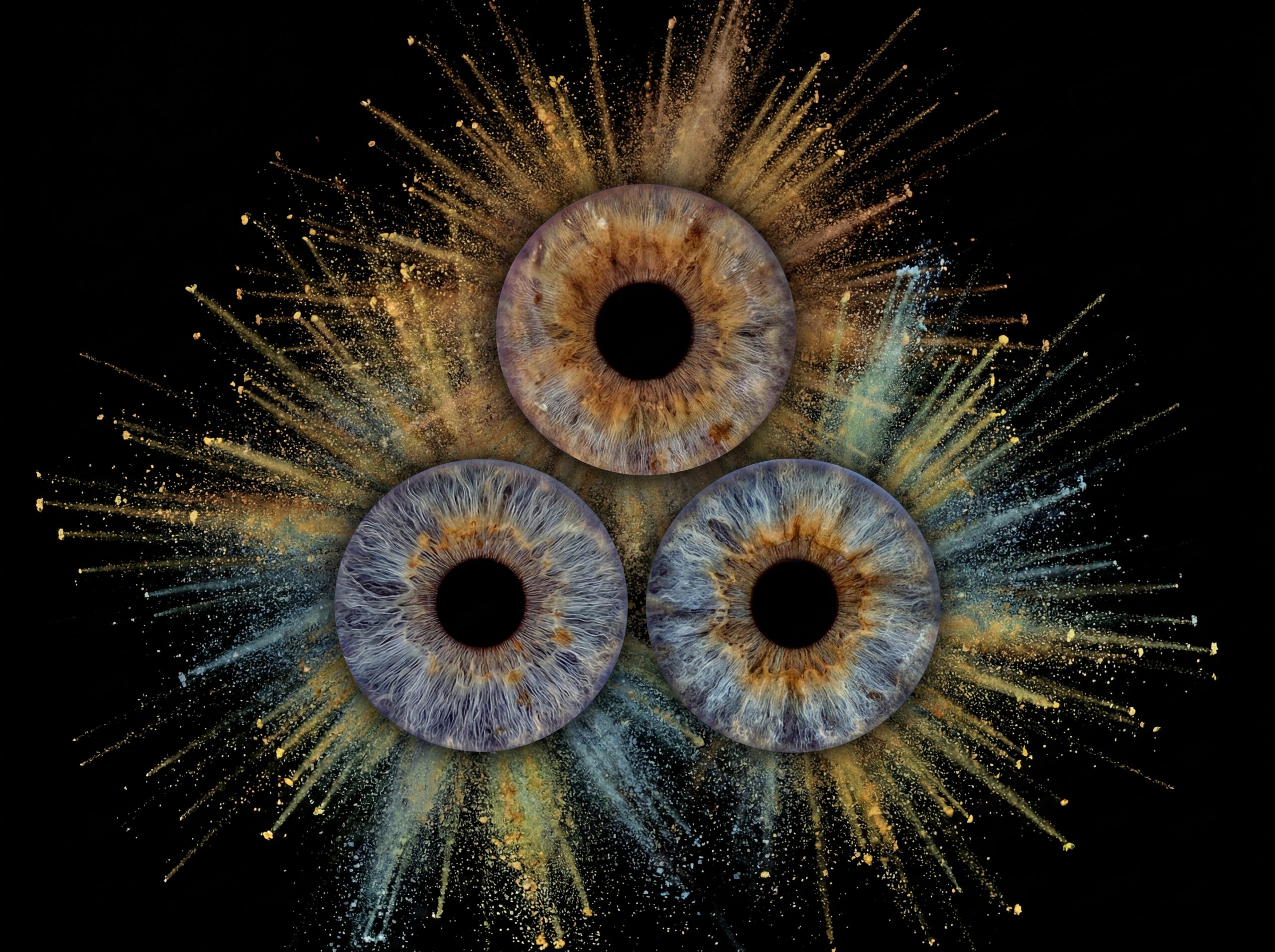 Powerful "Iris Art online" artwork: three human eye irises (grey-blue, yellowish, brown) joined by a powerful blue and yellowish dust explosion effect against a black background. This is unique iris art online, transforming the beauty of your eyes into an energetic and colorful masterpiece. The online iris service allows you to order such personalized artworks online.