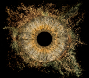Unique yellowish-brown human eye iris macro art with a powerful dusty particle explosion effect on a black background. This meaningful piece is part of the iris art online collection, symbolizing inner fire and energy. Order your online iris scan now and create an energetic accent for your home.